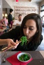 Beautiful girl with dark hair, dressed in black is eating green fresh algae salad with chopsticks in a restaurant