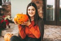 A beautiful girl with dark hair with makeup for the celebration of Halloween holds a pumpkin in her hands and smiles.