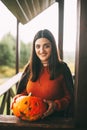 A beautiful girl with dark hair with makeup for the celebration of Halloween holds a pumpkin in her hands and smiles.