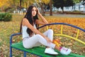 Beautiful girl with dark hair sits on a park bench holding yellow maple leaves in her hands, autumn sunny day, yellow leaves on Royalty Free Stock Photo