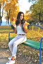 Beautiful girl with dark hair sits on a park bench holding yellow maple leaves in her hands, happy smile, autumn sunny day, yellow Royalty Free Stock Photo