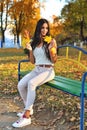 Beautiful girl with dark hair sits on a park bench holding yellow maple leaves in her hands, happy smile, autumn sunny day, yellow Royalty Free Stock Photo