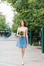 Beautiful girl in a delicate pink top and denim skirt outdoors. The girl holds a bouquet in her hands and walks Royalty Free Stock Photo