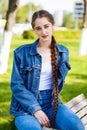 Beautiful girl in a denim jacket sits on a bench in a summer park