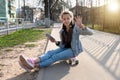 Beautiful girl in denim and pink sneakers with a phone in her hand sits on a penny board, a longboard. International Skateboarding Royalty Free Stock Photo