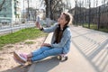 beautiful girl in denim and pink sneakers with a phone in her hand sits on a penny board, a longboard. Royalty Free Stock Photo