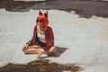 Beautiful girl devil sitting on city background near the puddle with his reflection. In anticipation of Halloween