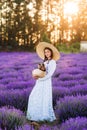 Beautiful girl with a dog in a basket in lavender. She`s wearing a long dress and a big hat