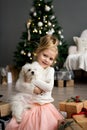 Beautiful girl with dog sitting near the Christmas tree. Merry Christmas and Happy Holidays. Royalty Free Stock Photo