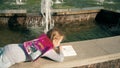 Beautiful girl draws in a notebook near the fountain
