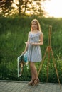 Beautiful girl draws a picture in the park using a palette with paints and a spatula. Easel and canvas with a picture. Summer is a Royalty Free Stock Photo