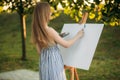 Beautiful girl draws a picture in the park using a palette with paints and a spatula. Easel and canvas with a picture. Summer is a Royalty Free Stock Photo