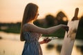 Beautiful girl draws a picture in the park using a palette with paints and a spatula. Easel and canvas with a picture. Summer is a Royalty Free Stock Photo