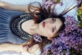 Beautiful girl in dress posing lying in lilac branches on a summer day, purple flowers in the Park. Spring portrait of a dreaming Royalty Free Stock Photo