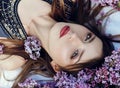 Beautiful girl in dress posing lying in lilac branches on a summer day, purple flowers in the Park. Spring portrait of a dreaming