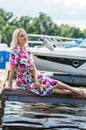 Beautiful girl in a dress is sitting on the pier against the backdrop of yachts in summer