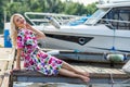 Beautiful girl in a dress is sitting on the pier against the backdrop of yachts in summer