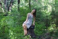 Beautiful girl in dress sitting on stump in forest