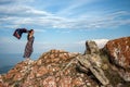 A beautiful girl in a dress with a waving scarf stands on a rock against a blue sky with clouds Royalty Free Stock Photo