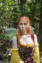 Beautiful girl dressed as a colorful yellow and orange fairy crossing her eyes and sticking out her tongue in a woodland setting a