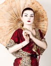 Beautiful girl dressed as a geisha girl holding a Chinese umbrella. Geisha makeup and hair dressed in a kimono. The