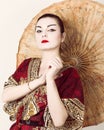 Beautiful girl dressed as a geisha girl holding a Chinese umbrella. Geisha makeup and hair dressed in a kimono. The