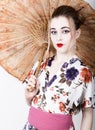 Beautiful girl dressed as a geisha girl holding a Chinese umbrella. Geisha makeup and hair dressed in a kimono. The