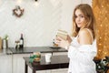 Beautiful girl dressed in a white shirt holding a gift in modern bright kitchen