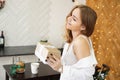 Beautiful girl dressed in a white shirt holding a gift in modern bright kitchen