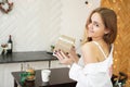 Beautiful girl dressed in a white shirt holding a gift in modern bright kitchen