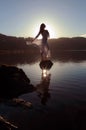 Beautiful Girl dressed in white, silhouetted by the sun reflected in still lake