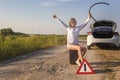 Beautiful girl driver sits on an empty canister for gasoline next to a broken car while waiting for help on a rural road