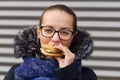 Beautiful girl eagerly eats a hamburger on the street