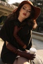 Beautiful girl in elegant coat and hat drinking coffee at park Royalty Free Stock Photo