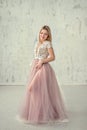 Beautiful girl in an evening dress with lace and pink fartine on the background of a white textural wall. Royalty Free Stock Photo