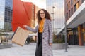 Beautiful girl in eyeglasses is holding shopping bags, looking at camera and smiling while walking down the street. Royalty Free Stock Photo