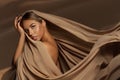 Beautiful Girl Face with Natural Makeup and Sun Tanned Skin. Beauty Woman wrapped in Brown Silk Fabric waving on Wind. Fashion