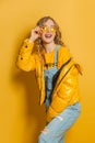 Beautiful girl fashion model in winter jacket and sunglasses standing on bright yellow background Royalty Free Stock Photo