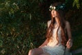 Beautiful girl in floral wreath is sitting outdoors