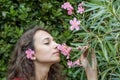 A beautiful girl with a flower in her hair smells pink oleander flowers with her eyes closed