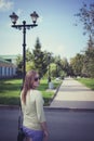 Beautiful girl with flowing hair in short shorts and glasses on the background of an asphalt path with a lantern