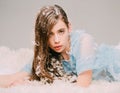 Beautiful girl with fluff in her hair lying on downy bed full of feathers, bedtime fantasy. Young female in blue dress Royalty Free Stock Photo