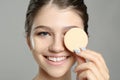 Beautiful girl with foundation smear on her face holding sponge against grey background, closeup Royalty Free Stock Photo