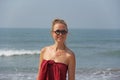 Beautiful girl freak in a red dress and blond hair, on the background of the sea. Summer girl in round wooden glasses. Unusual Royalty Free Stock Photo