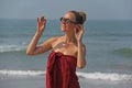 Beautiful girl freak in a red dress and blond hair, on the background of the sea. Summer girl in round wooden glasses. Unusual Royalty Free Stock Photo