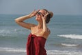 Beautiful girl freak in a red dress and blond hair, on the background of the sea. Summer girl in round wooden glasses. Unusual Royalty Free Stock Photo