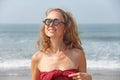 Beautiful girl freak in a red dress and blond hair, on the background of the sea. Summer girl in round wooden glasses. Unusual