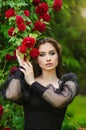 Beautiful girl in the garden with roses. Portrait of a woman with big lips in black clothes on a background of red flowers. Greens Royalty Free Stock Photo