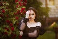 Beautiful girl in the garden with roses. Portrait of a woman with big lips in black clothes on a background of red flowers. Greens Royalty Free Stock Photo