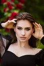 Beautiful girl in the garden with roses. Portrait of a woman with big lips in black clothes on a background of red flowers. Greens Royalty Free Stock Photo